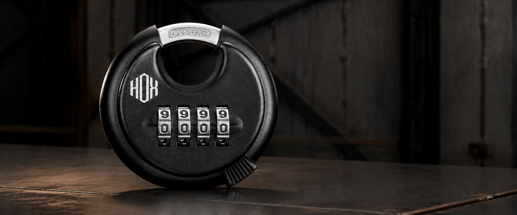 Black HOX four-digit combination disc padlock on a dark metal surface in a shed-inspired setting.